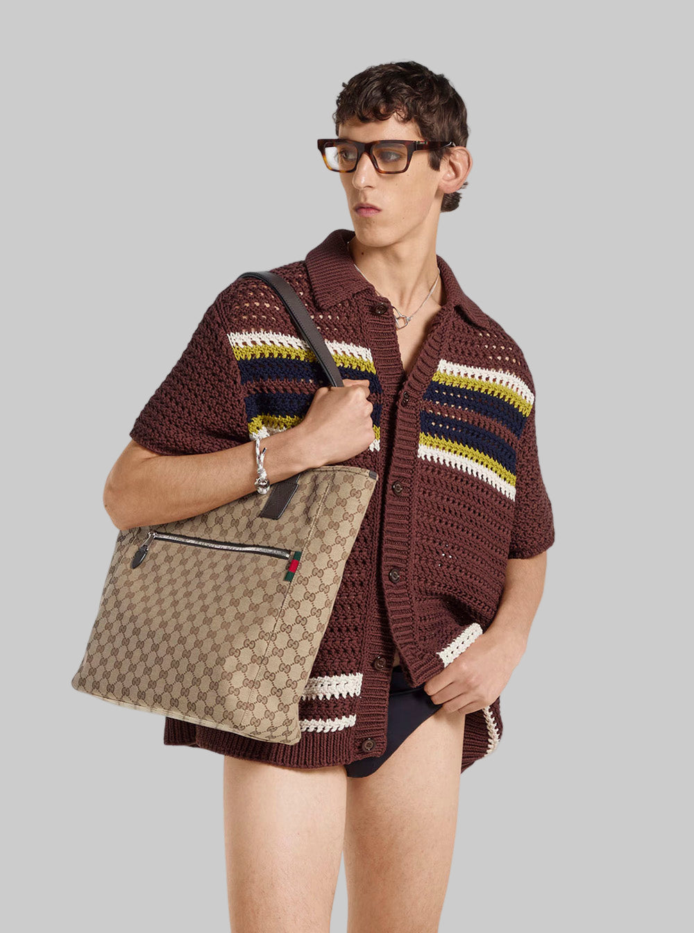 Person wearing a brown patterned cardigan holding a Gucci bag on a white background