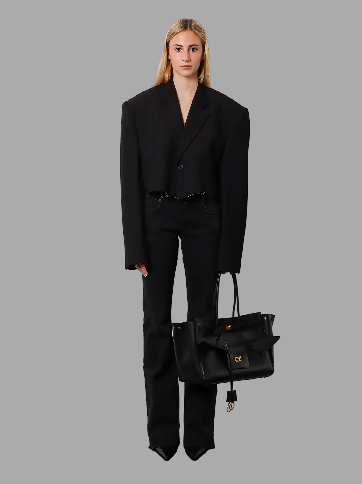 Person wearing a black suit holding a matching black handbag against a white background
