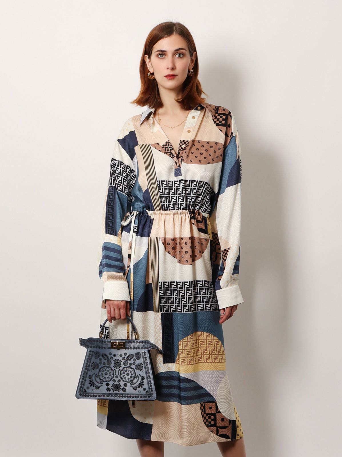Woman wearing a patchwork dress holding a handbag against a white background